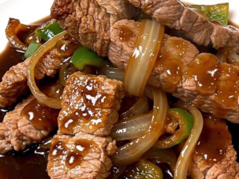 A top-down view of tender pork loin strips with onions and peppers in a dark, savory black pepper sauce.