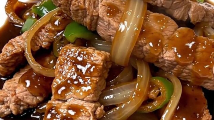 A top-down view of tender pork loin strips with onions and peppers in a dark, savory black pepper sauce.
