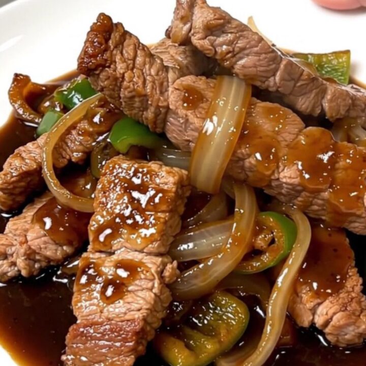 A top-down view of tender pork loin strips with onions and peppers in a dark, savory black pepper sauce.