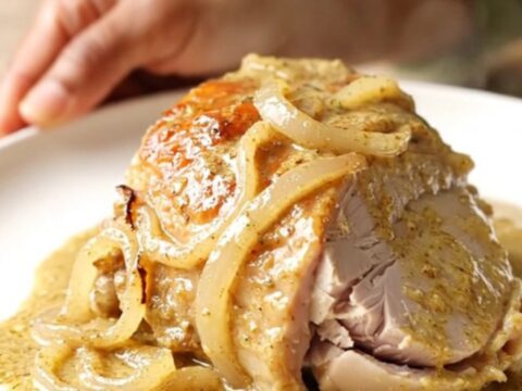 A close-up of creamy Dijon turkey tenderloin with onions in a black slow cooker.