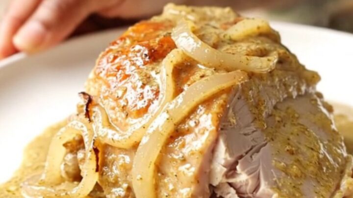A close-up of creamy Dijon turkey tenderloin with onions in a black slow cooker.