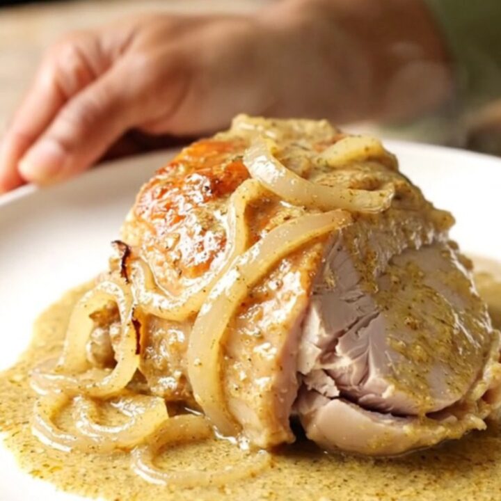 A close-up of creamy Dijon turkey tenderloin with onions in a black slow cooker.