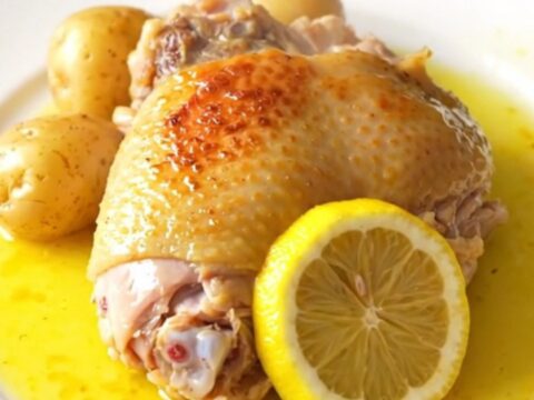 A high-angle shot of skinless bone-in turkey thighs, baby potatoes, and lemon slices in a slow cooker.