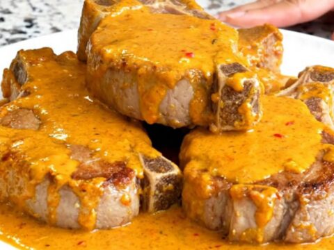 A close-up of tender pork chops smothered in a rich, orange pimento cheese sauce served on a white plate.