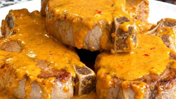 A close-up of tender pork chops smothered in a rich, orange pimento cheese sauce served on a white plate.