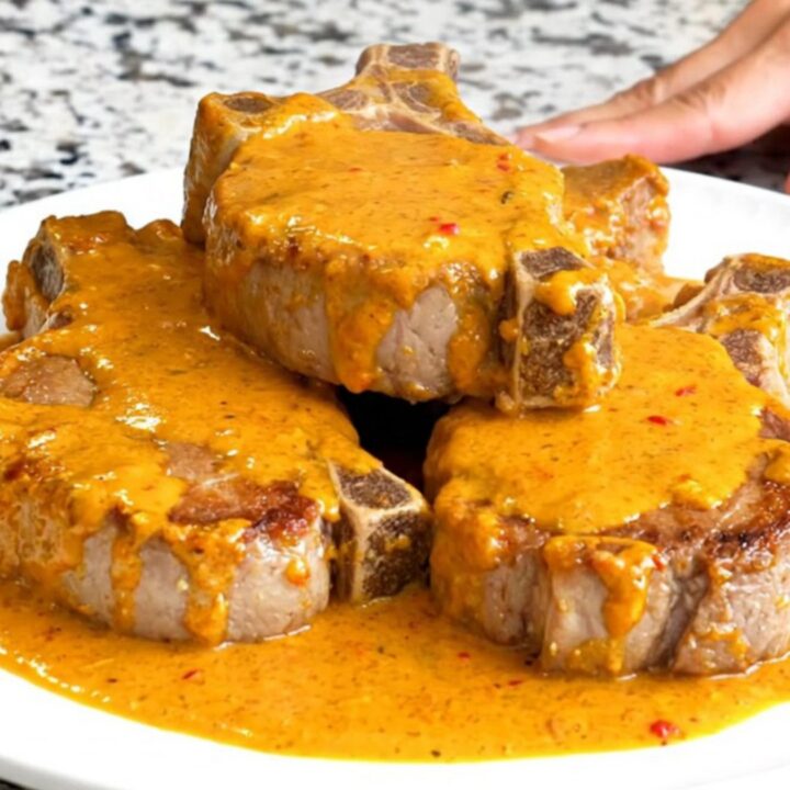 A close-up of tender pork chops smothered in a rich, orange pimento cheese sauce served on a white plate.