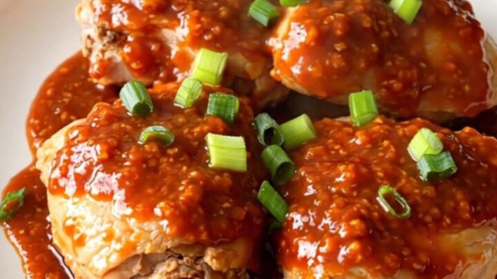 A bowl filled with tender chicken thighs glazed in a glossy honey chili sauce with green onions.