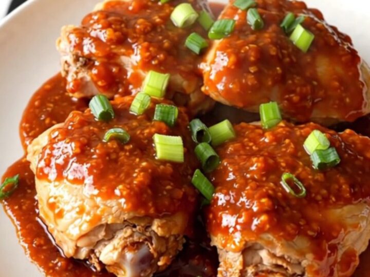 A bowl filled with tender chicken thighs glazed in a glossy honey chili sauce with green onions.