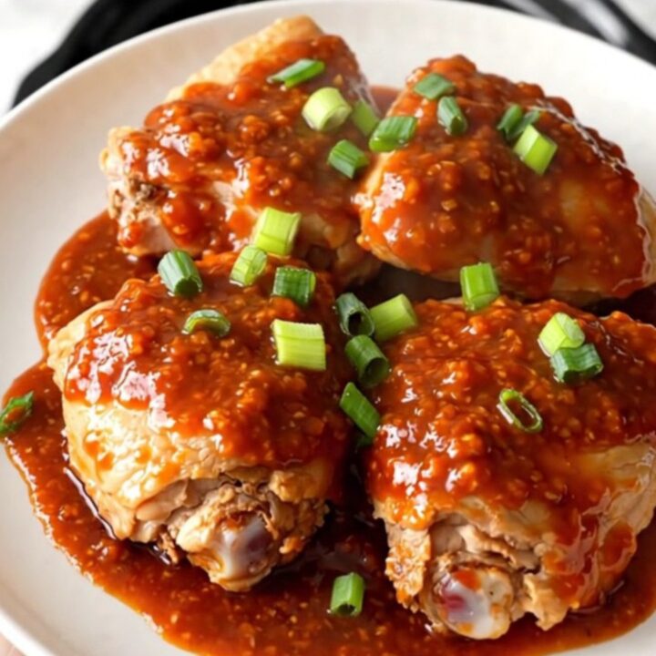 A bowl filled with tender chicken thighs glazed in a glossy honey chili sauce with green onions.