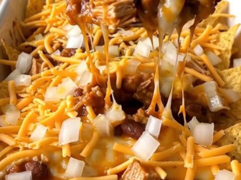 A top-down view of a turkey chili corn chip pie in a white ceramic dish, with melted cheese and fresh onions.