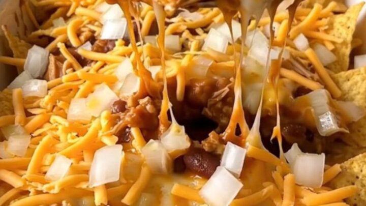 A top-down view of a turkey chili corn chip pie in a white ceramic dish, with melted cheese and fresh onions.