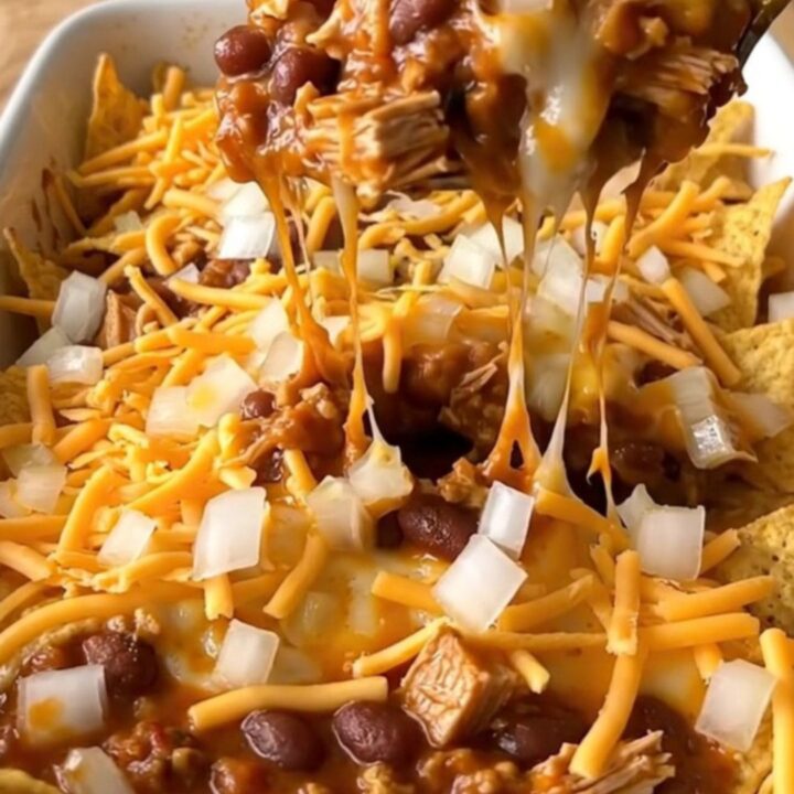 A top-down view of a turkey chili corn chip pie in a white ceramic dish, with melted cheese and fresh onions.
