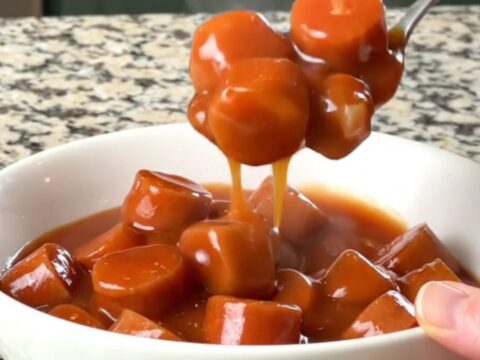 A slow cooker filled with sliced hot dogs and beans in a rich, thick, brown sauce.