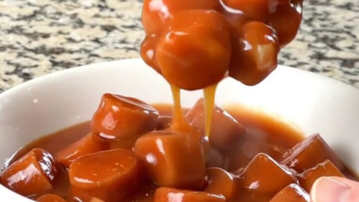 A slow cooker filled with sliced hot dogs and beans in a rich, thick, brown sauce.