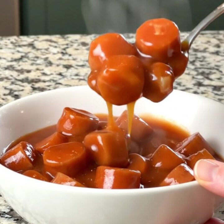 A slow cooker filled with sliced hot dogs and beans in a rich, thick, brown sauce.
