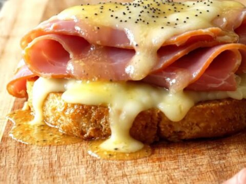 A close-up of the slow cooker filled with layers of deli ham, melted Swiss cheese, and poppy seeds in a buttery sauce.