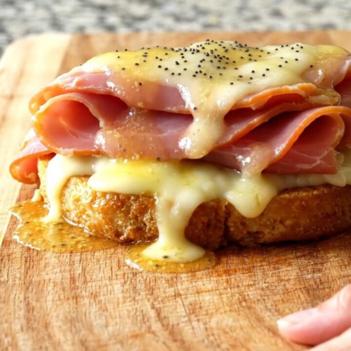 A close-up of the slow cooker filled with layers of deli ham, melted Swiss cheese, and poppy seeds in a buttery sauce.