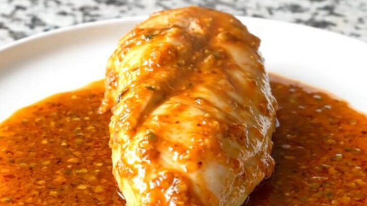 A close-up of tender, cooked chicken breasts glazed in a rich, orange-red smoky honey lime sauce inside a black slow cooker.