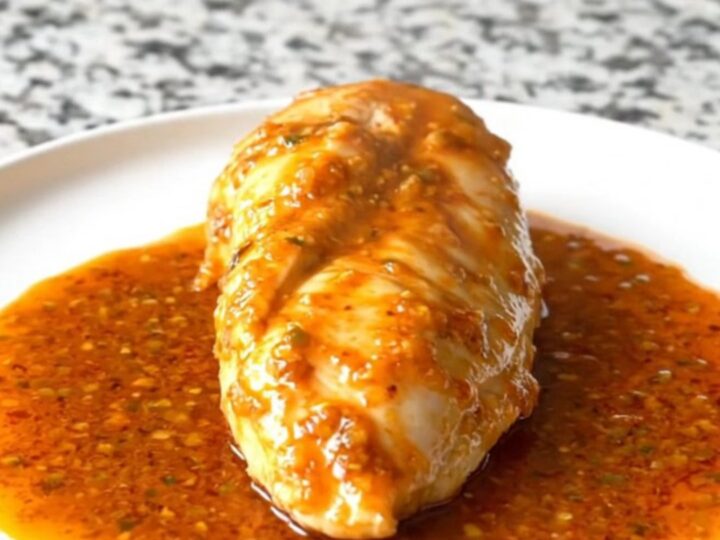 A close-up of tender, cooked chicken breasts glazed in a rich, orange-red smoky honey lime sauce inside a black slow cooker.