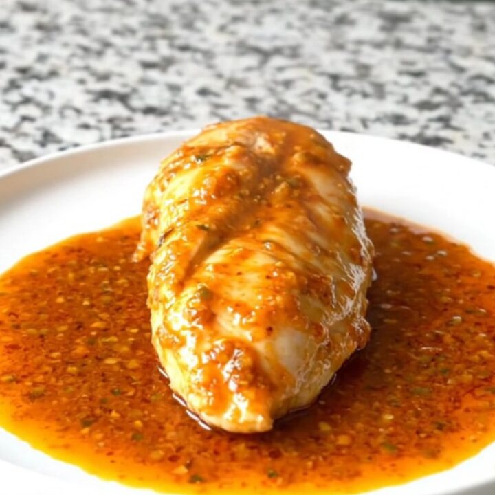 A close-up of tender, cooked chicken breasts glazed in a rich, orange-red smoky honey lime sauce inside a black slow cooker.