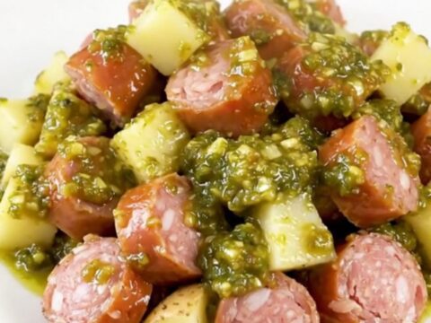 A rustic slow cooker filled with golden potatoes and sliced smoked sausage in a vibrant green salsa sauce.