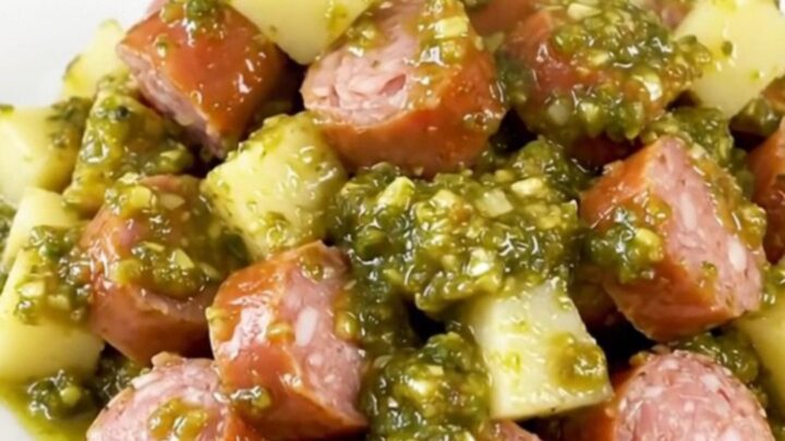 A rustic slow cooker filled with golden potatoes and sliced smoked sausage in a vibrant green salsa sauce.