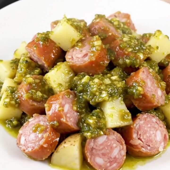 A rustic slow cooker filled with golden potatoes and sliced smoked sausage in a vibrant green salsa sauce.