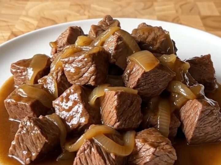 A close-up of tender beef tips in a rich brown gravy served on a white plate.