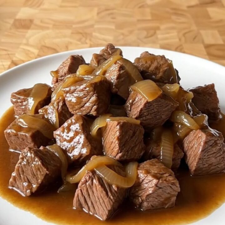 A close-up of tender beef tips in a rich brown gravy served on a white plate.