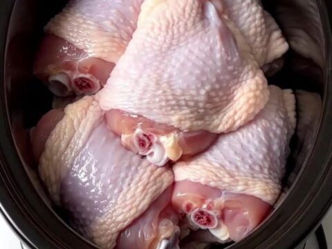 A close-up of tender, shredded turkey carnitas in a slow cooker with visible citrus and onions.