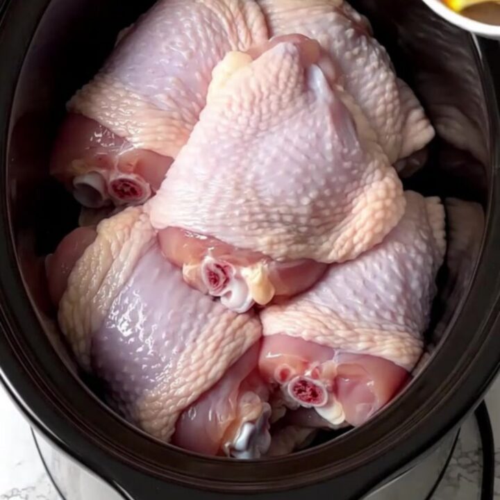 A close-up of tender, shredded turkey carnitas in a slow cooker with visible citrus and onions.