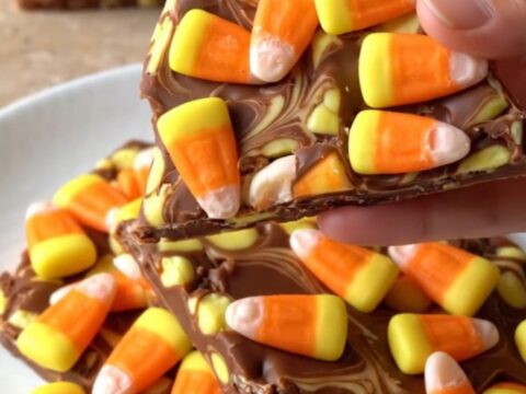 A large piece of white chocolate bark topped with candy corn and orange swirls on a dark baking sheet.