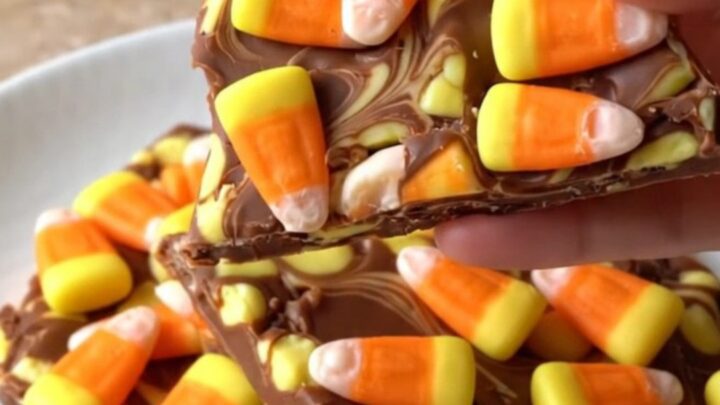 A large piece of white chocolate bark topped with candy corn and orange swirls on a dark baking sheet.