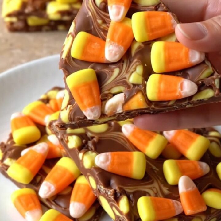 A large piece of white chocolate bark topped with candy corn and orange swirls on a dark baking sheet.