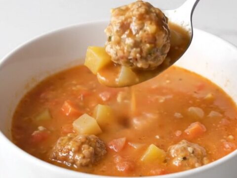 A bowl of creamy tomato soup with whole turkey meatballs and soft vegetables, garnished with herbs.