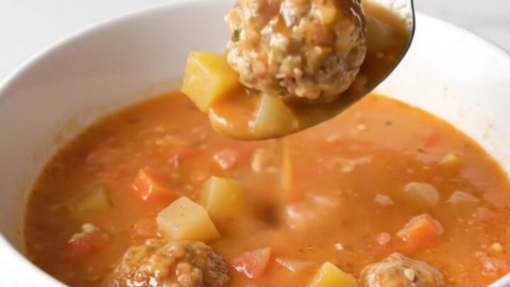 A bowl of creamy tomato soup with whole turkey meatballs and soft vegetables, garnished with herbs.