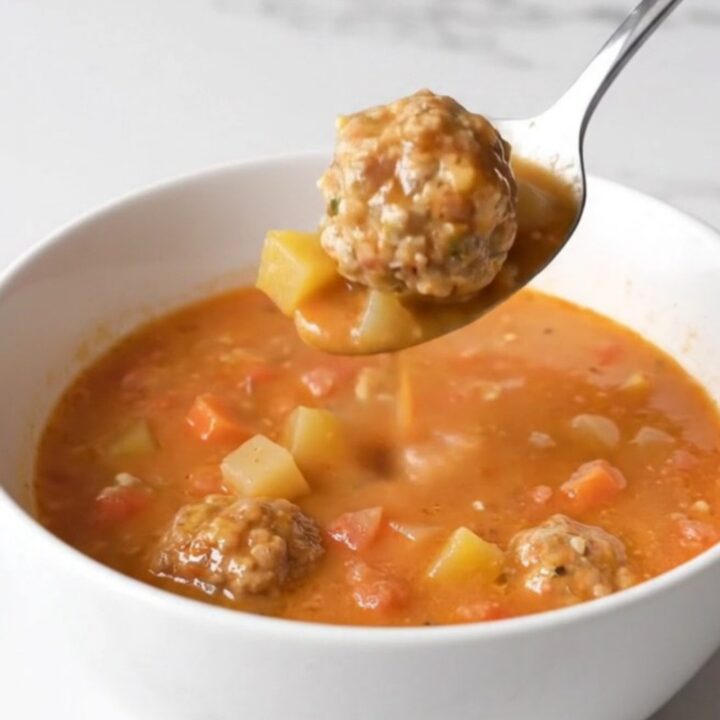 A bowl of creamy tomato soup with whole turkey meatballs and soft vegetables, garnished with herbs.