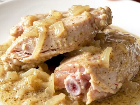 A close-up of tender, braised turkey tenderloins covered in thick, creamy peppered gravy on a white plate.