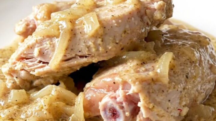 A close-up of tender, braised turkey tenderloins covered in thick, creamy peppered gravy on a white plate.