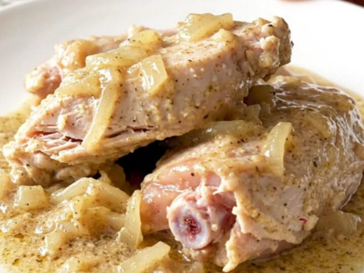 A close-up of tender, braised turkey tenderloins covered in thick, creamy peppered gravy on a white plate.