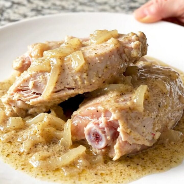 A close-up of tender, braised turkey tenderloins covered in thick, creamy peppered gravy on a white plate.