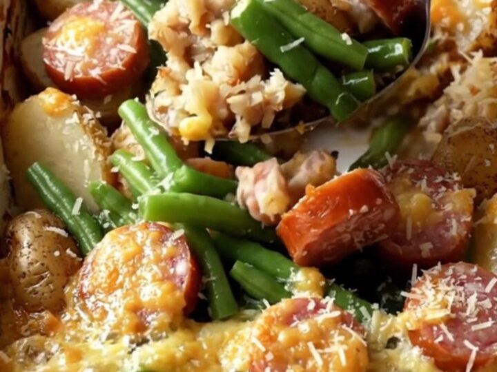 A top-down view of a rectangular ceramic dish filled with potatoes, green beans, and sausage.