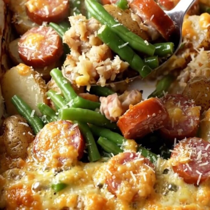 A top-down view of a rectangular ceramic dish filled with potatoes, green beans, and sausage.