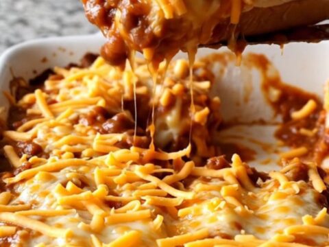 A close-up view of a chili cheese dog bake featuring melted cheddar cheese and hearty chili in a ceramic dish.
