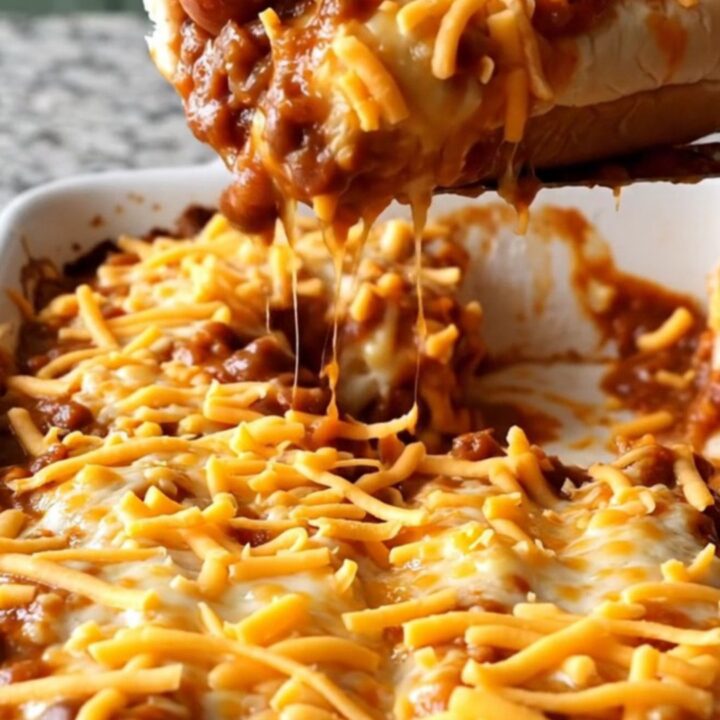 A close-up view of a chili cheese dog bake featuring melted cheddar cheese and hearty chili in a ceramic dish.