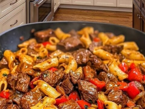 A close-up view of a skillet filled with penne pasta, seared steak cubes