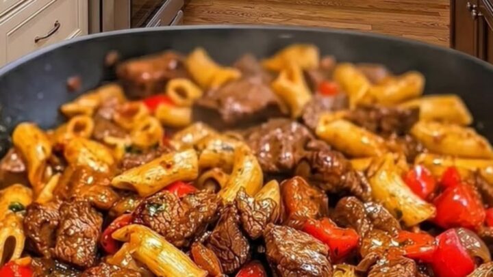 A close-up view of a skillet filled with penne pasta, seared steak cubes