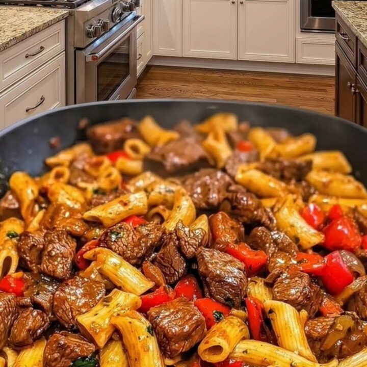 A close-up view of a skillet filled with penne pasta, seared steak cubes