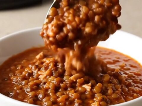 A warm bowl of slow cooker turkey and lentil chili with steam rising, set on a beige kitchen counter.