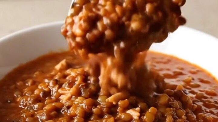 A warm bowl of slow cooker turkey and lentil chili with steam rising, set on a beige kitchen counter.